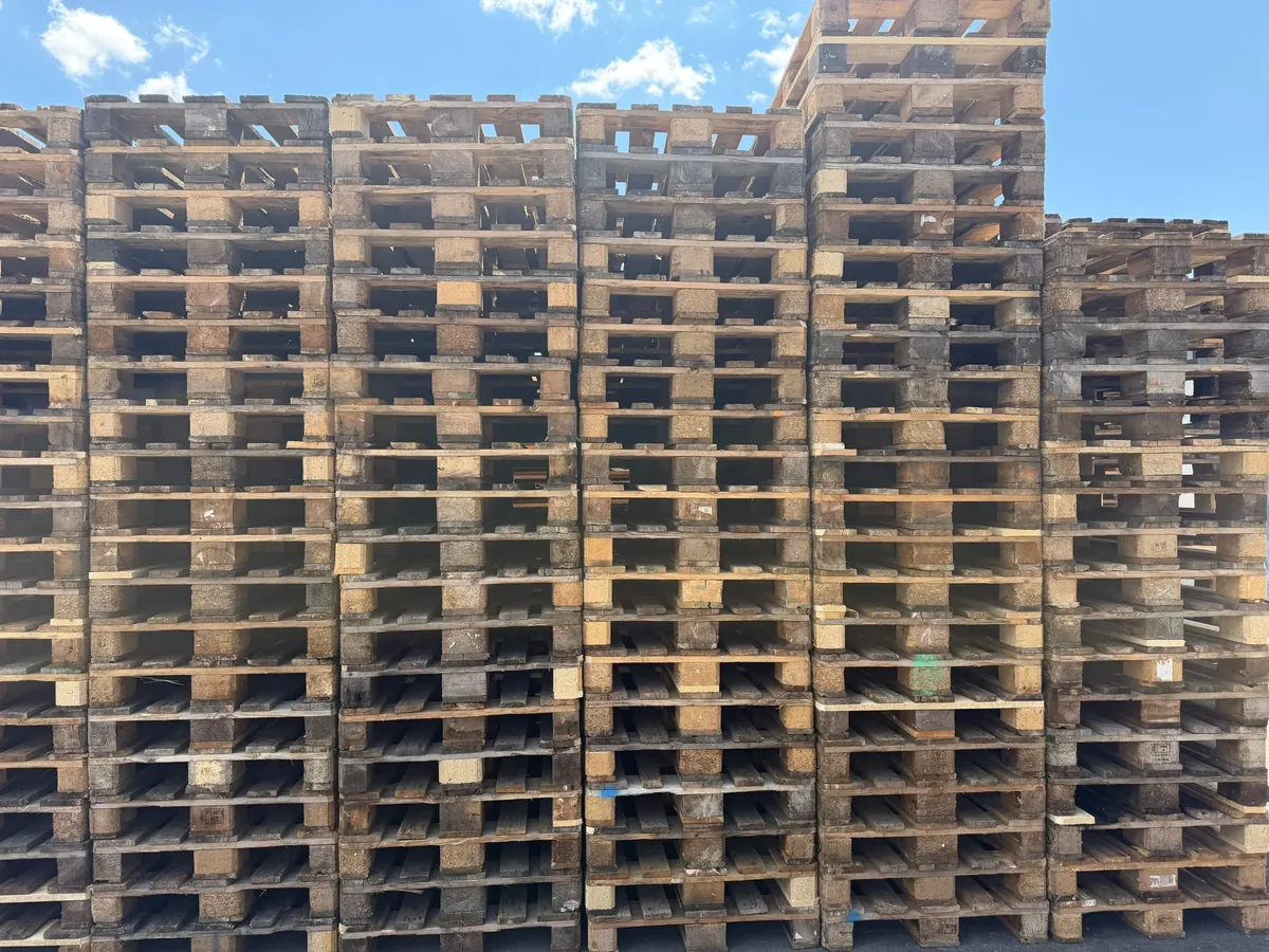 Wysokie stosy palet z silnymi śladami użytkowania, przygotowane do oceny i odkupu